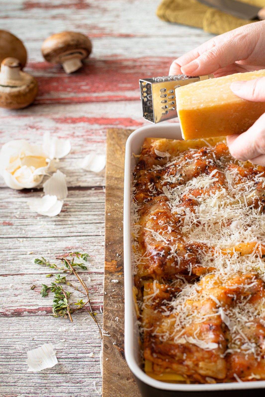 A hand grating Parmigiano Reggiano over a tray of lasagna