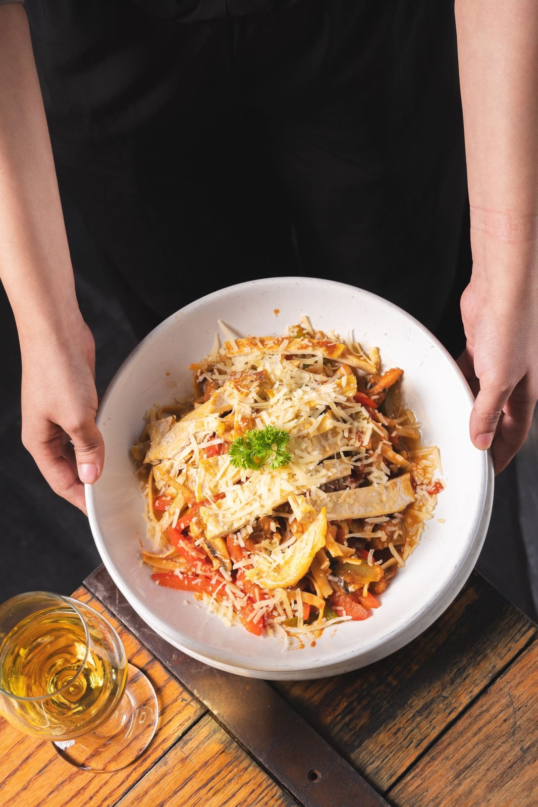 Two hands holding a bowl of pasta covered in grated Parmigiano Reggiano