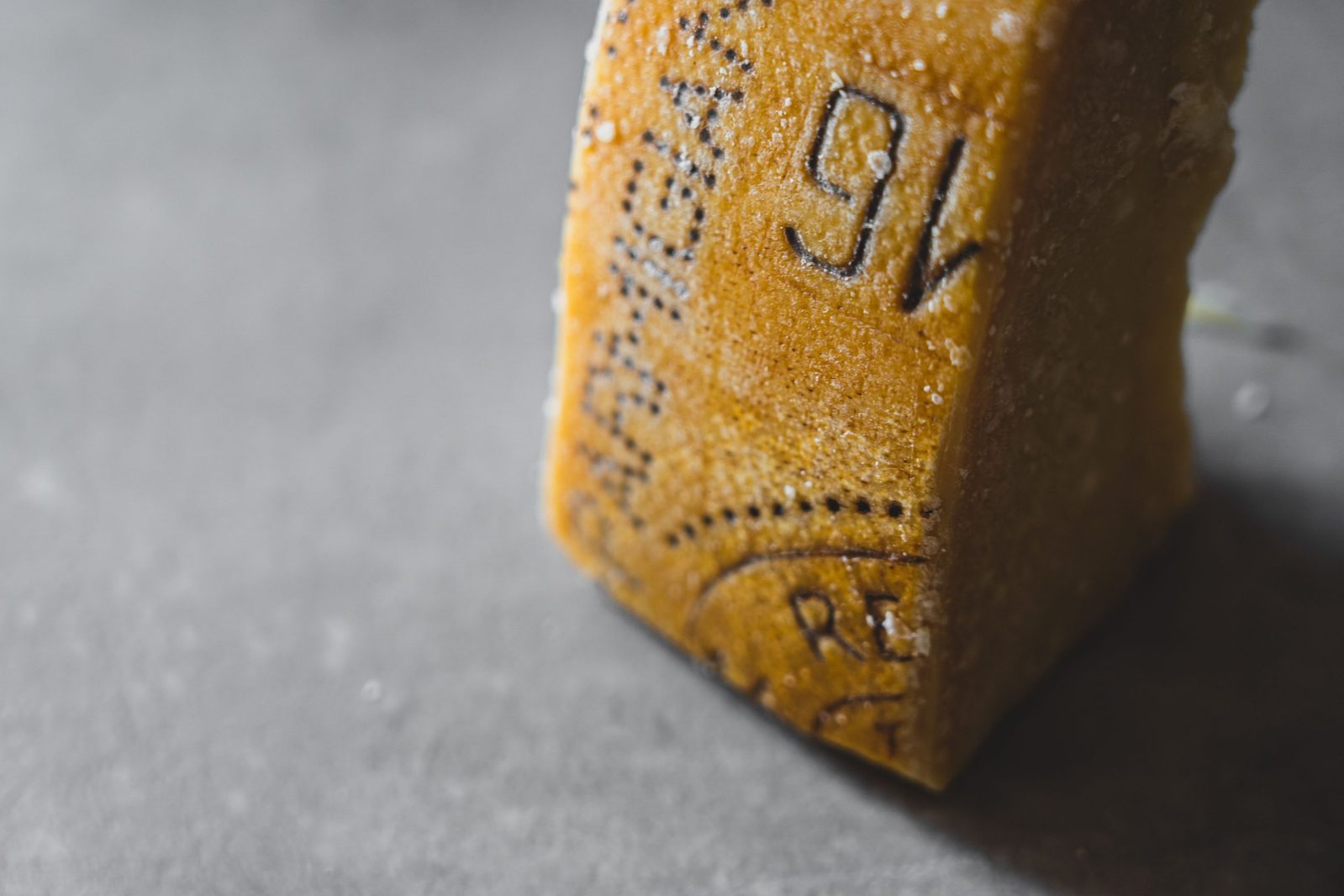A wedge of Parmigiano Reggiano showing the dairy number and the letters RE on its rind